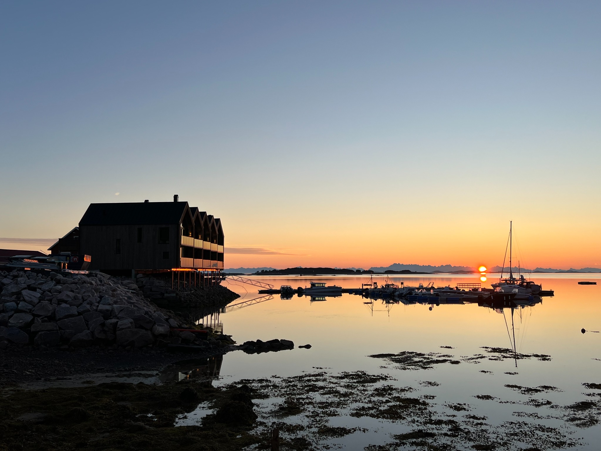 Waterfront buildings with pitched roofs and balconies beside a marina at sunset