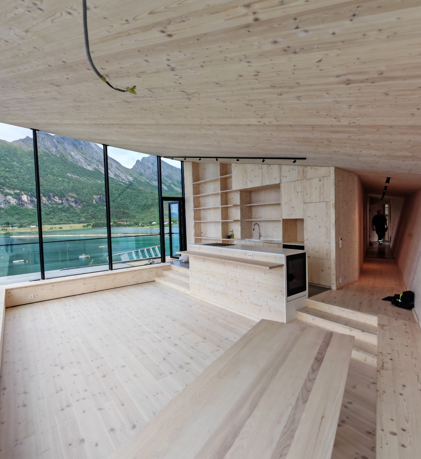 Interiør under utførelse på Bergtatt, med synlig tre, kjøkkenøy og store glassflater mot sjøen og fjellene